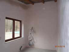 Omítnutá místnost s dřevěným stropem a oknem s výhledem na bazén