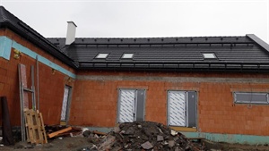 Exteriér domu s cihlovým obkladem, novou střechou a stavební sutí