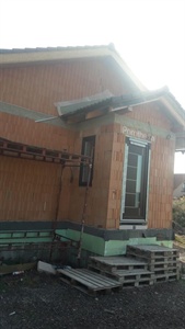 Exteriér domu s dřevěným obkladem, vchodové dveře a naskládané palety