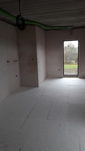 Místnost s polystyrenovými deskami na podlaze a prosklenými dveřmi do zahrady
