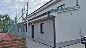 Fasáda budovy u sportoviště po zateplení, pohled od oplocení kurtu