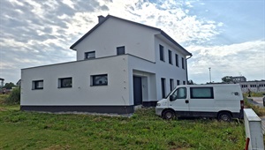 Patrový rodinný dům s bílou zateplenou fasádou a tmavým soklem