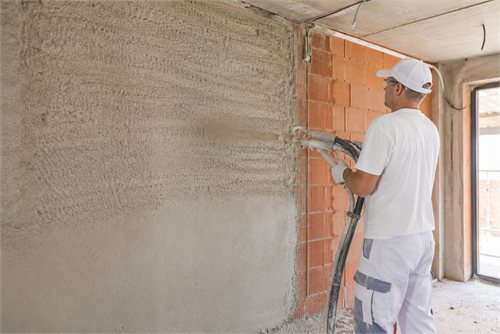 Pracovník nanáší strojní omítku na cihlovou zeď pomocí stříkací pistole